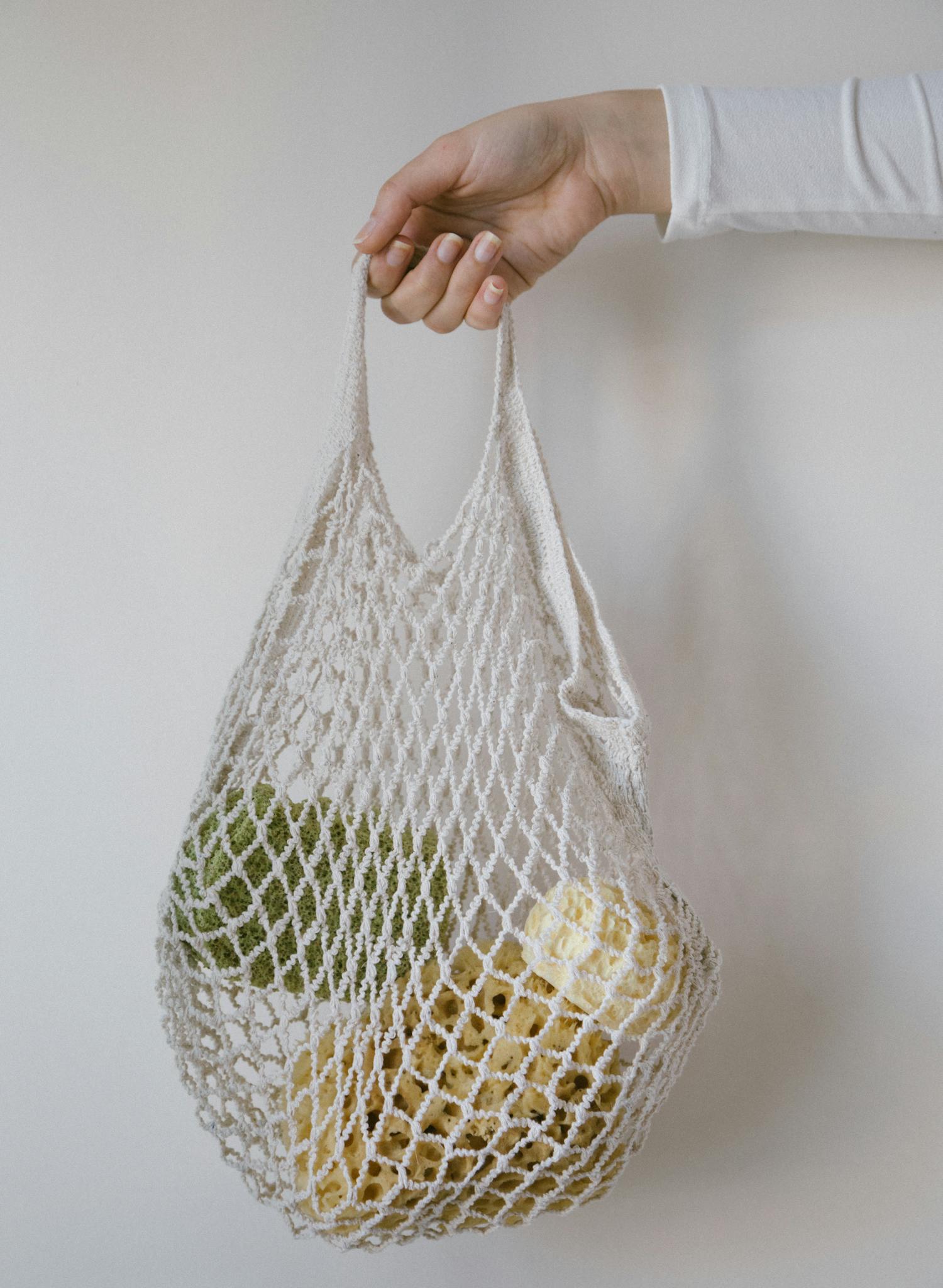 A hand holding a mesh bag filled with fresh produce promotes eco-friendly shopping.