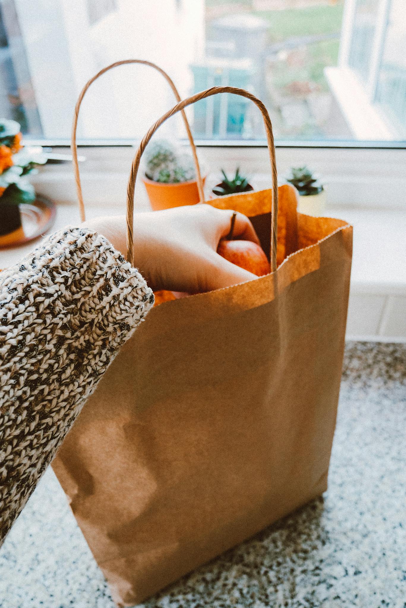 Close-up of a hand taking groceries from a paper bag on a kitchen countertop.