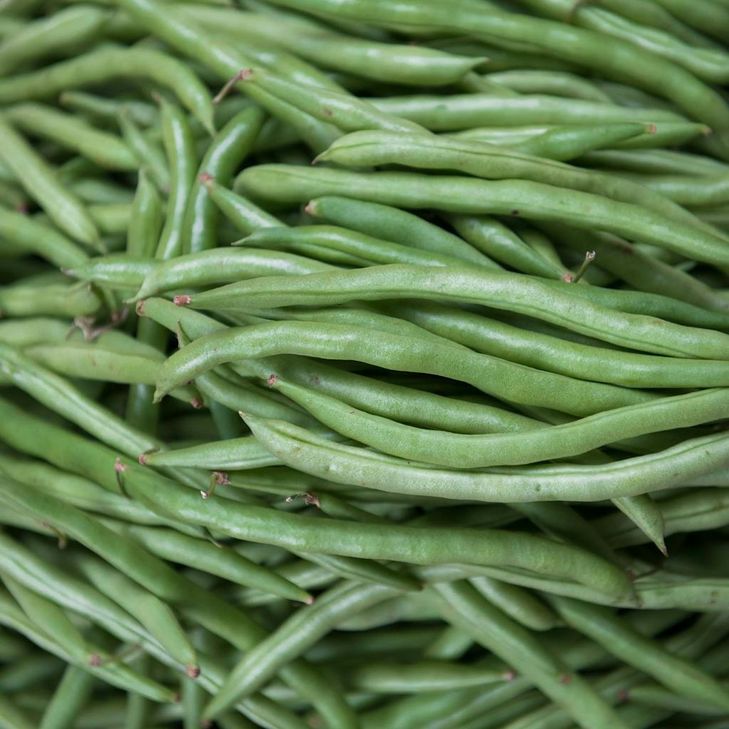 Vibrant pile of fresh organic green beans at a market stall, captured close-up for rich texture and color.